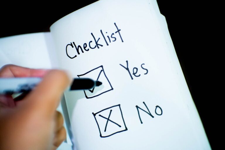 Ein handgeschriebener Checklisteneintrag in einem geöffneten Notizbuch, wobei das Wort 'Checklist' oben auf der Seite steht und zwei Auswahlmöglichkeiten darunter angeboten werden: 'Yes' mit einem Häkchen in der Box und 'No' mit einem X in der Box. Eine Hand hält einen Stift, der gerade das 'Yes' angekreuzt hat.
