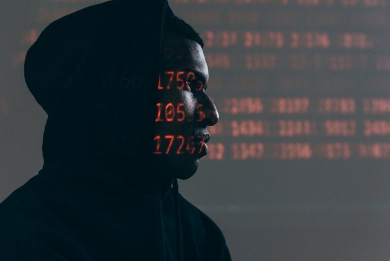 Silhouette einer Person mit Kapuze vor einem Hintergrund mit roten digitalen Zahlen, die eine Ransomware-Cybersecurity-Bedrohung symbolisiert.