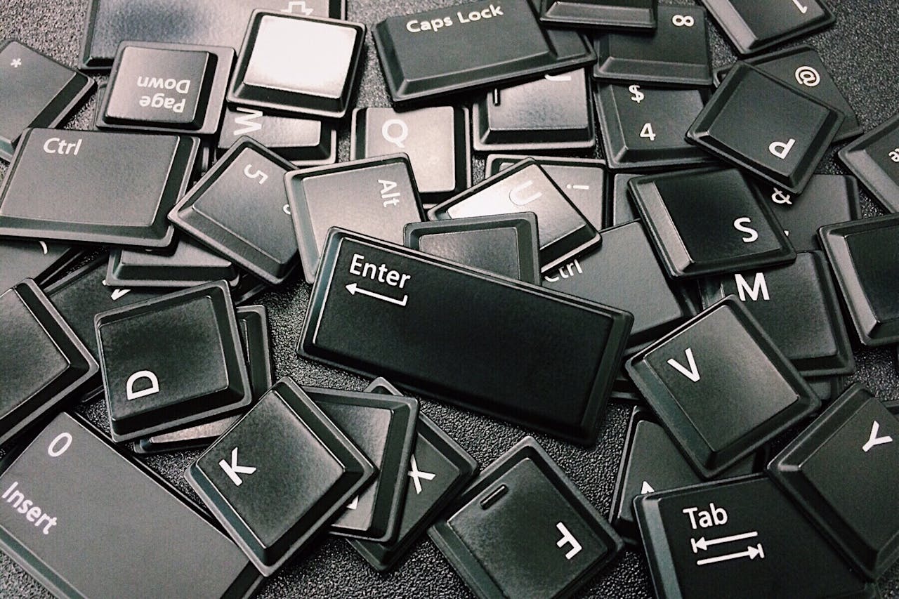 Eine Anhäufung von schwarzen Tastaturtasten, die verstreut auf einer Oberfläche liegen, wobei Schlüssel wie "Enter", "Ctrl" und "Caps Lock" deutlich erkennbar sind.