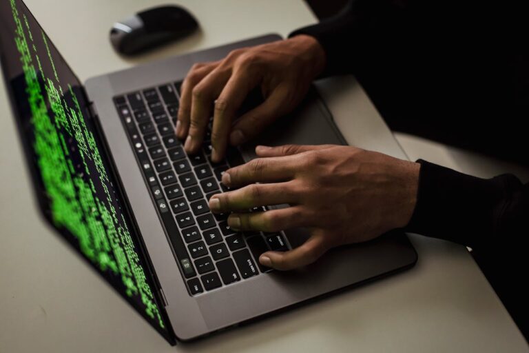 Person tippt auf einer Laptop-Tastatur mit grünem Code auf dem Bildschirm im Hintergrund.