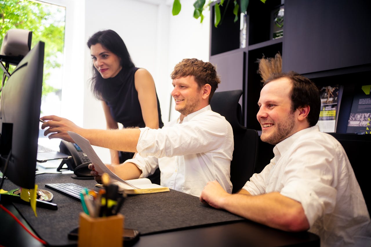 Drei Personen in einem Büro arbeiten zusammen an einem PC, während sie auf den Bildschirm schauen. Der Fokus liegt auf einer möglichen PC-Reparatur, bei der ein Team technische Unterstützung bietet.