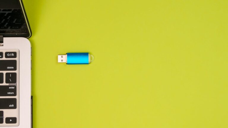 Ein blauer USB-Stick liegt neben einem silbernen Laptop auf einer grünen Oberfläche, bereit zum Anschließen an den Computer.